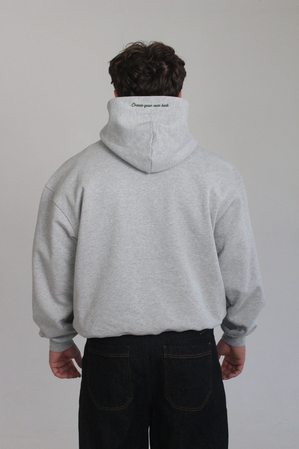 Model is wearing the hamby hoodie in ash grey. Plain back of hoodie but with ‘Create your own luck’ embroidered on the hood in green. 