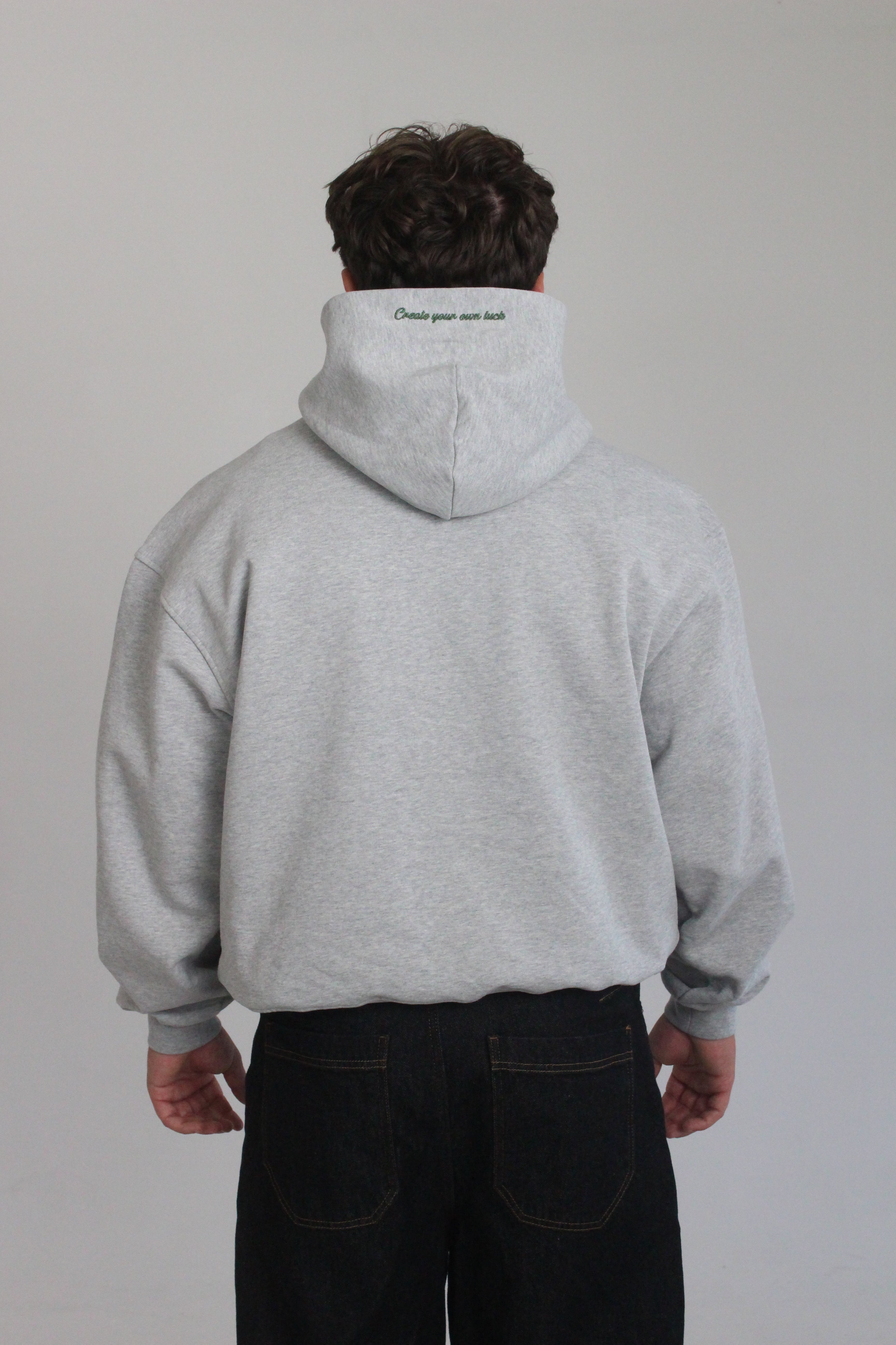Model is wearing the hamby hoodie in ash grey. Plain back of hoodie but with ‘Create your own luck’ embroidered on the hood in green. 