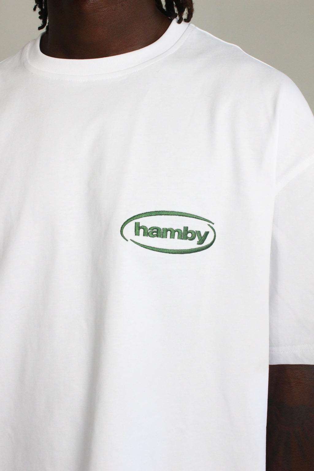 Close up of white t-shirt with hamby logo embroidered on the front left chest in green. 