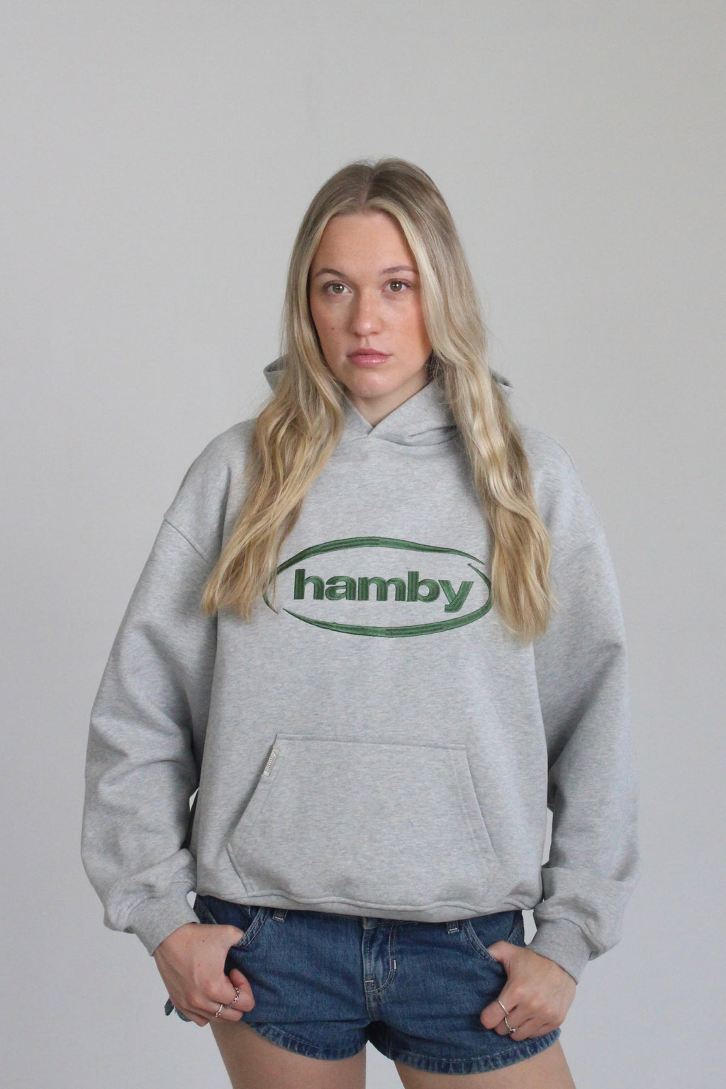 Model is wearing the hamby hoodie in ash grey. Hamby logo embroidery on centre chest in green. Hoodie is 480gsm, 100% cotton and it’s an oversize, slightly boxy fit. 