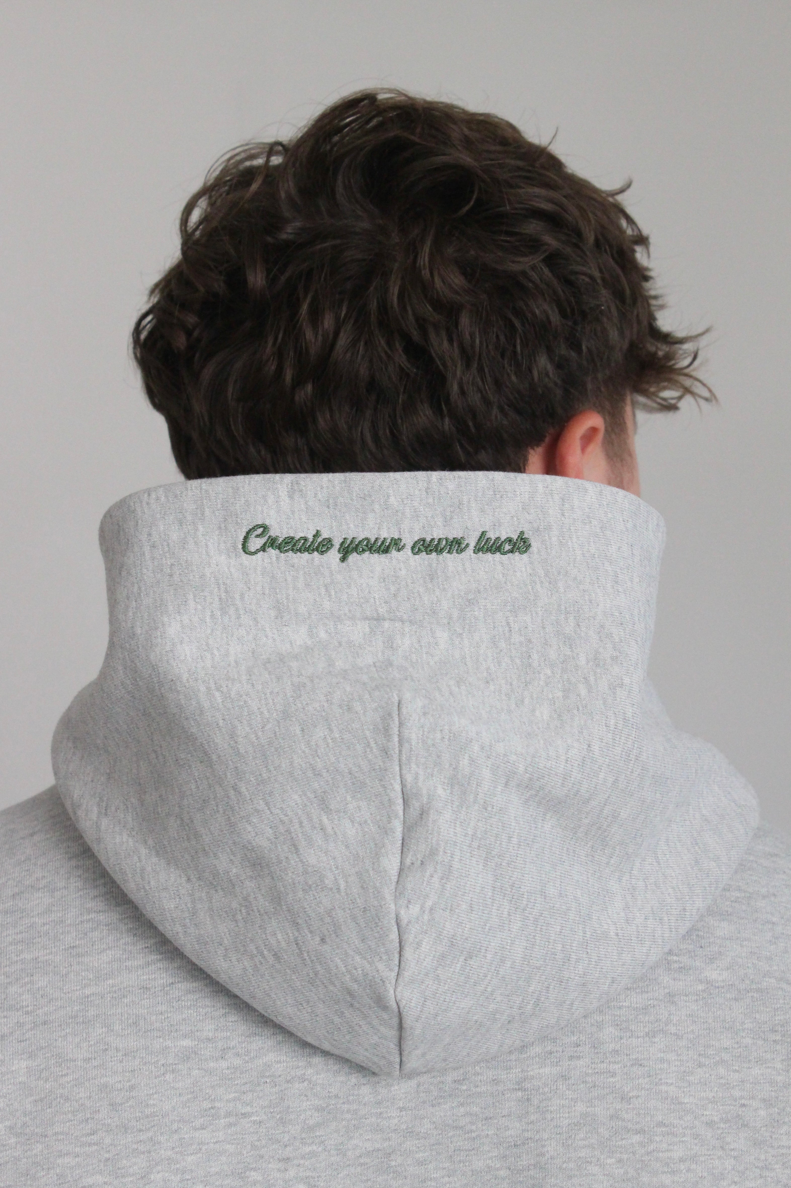 Shows model wearing the hamby hoodie. Close up of the ‘Create your own luck’ embroidery on the hood in green. 