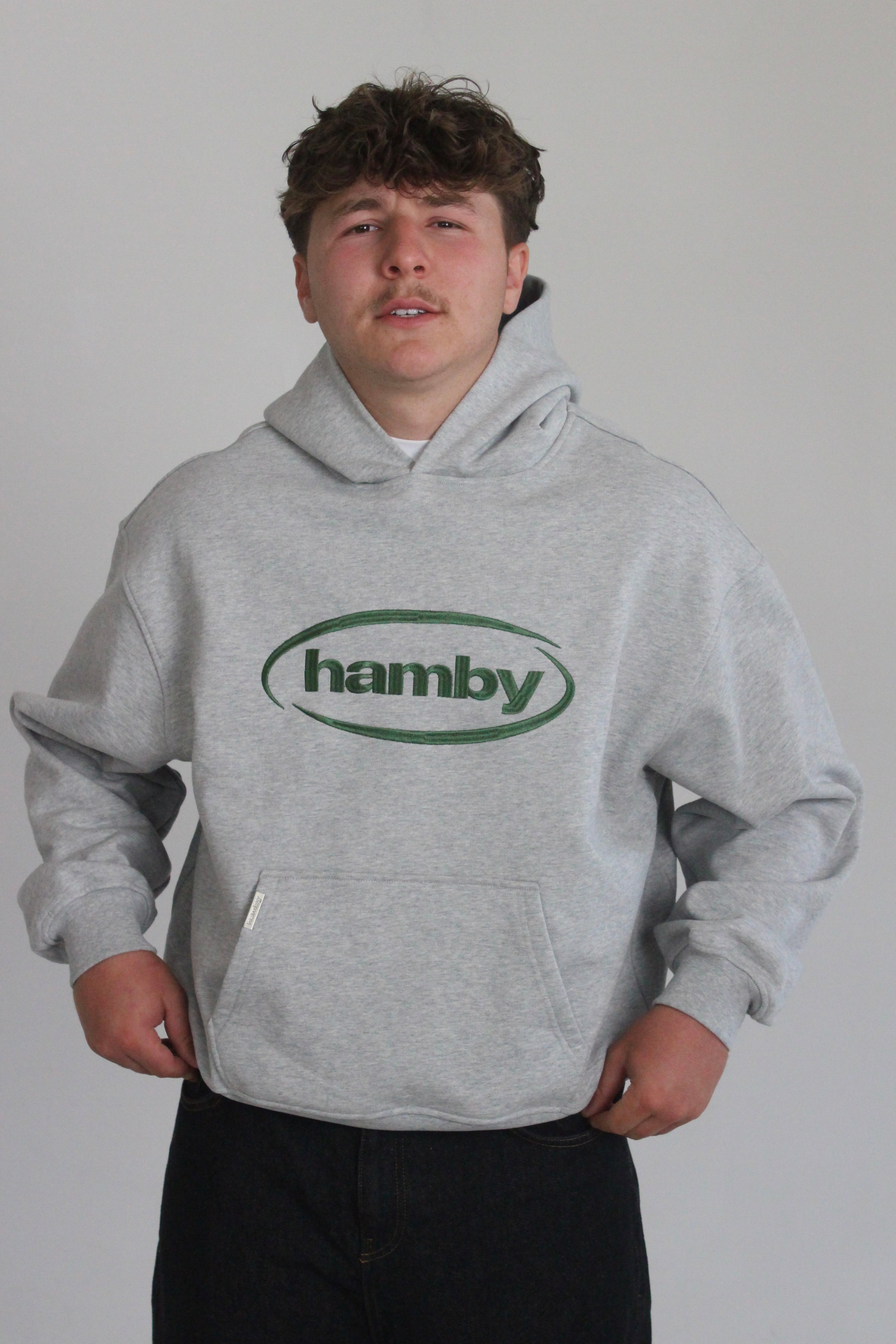 Model is wearing the hamby hoodie in ash grey. Hamby logo embroidery on centre chest in green. Hoodie is 480gsm, 100% cotton and it’s an oversize, slightly boxy fit. 