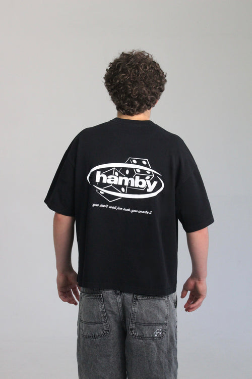 Model wearing the roll the dice tee by hamby in black. The hamby logo screen printed on the back with the signature dice. Then an embroidered quote underneath to complete the design on the heavyweight t-shirt. Quote- ‘you don’t wait for luck, you create it’