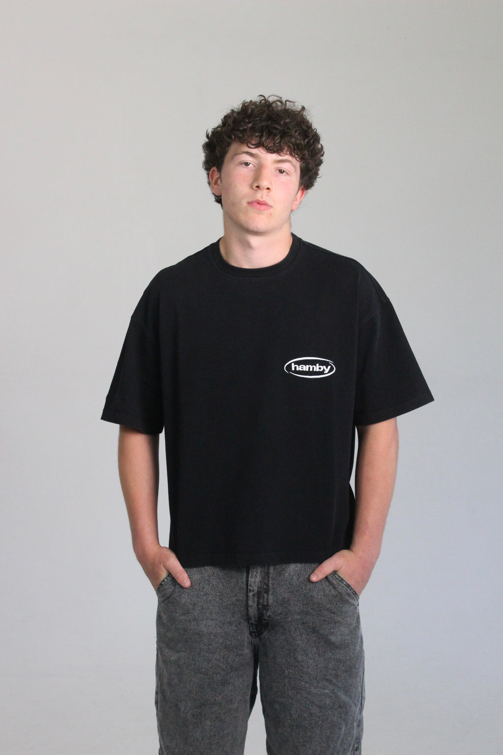 Model wearing boxy oversize hamby black t-shirt with hamby logo embroidered on the front left chest in white. T-shirt is 100% cotton, 240gsm. 