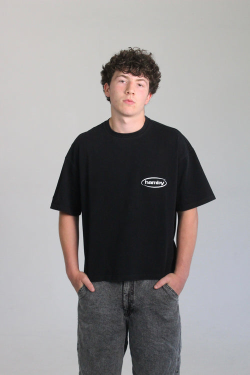 Model wearing boxy oversize hamby black t-shirt with hamby logo embroidered on the front left chest in white. T-shirt is 100% cotton, 240gsm. 