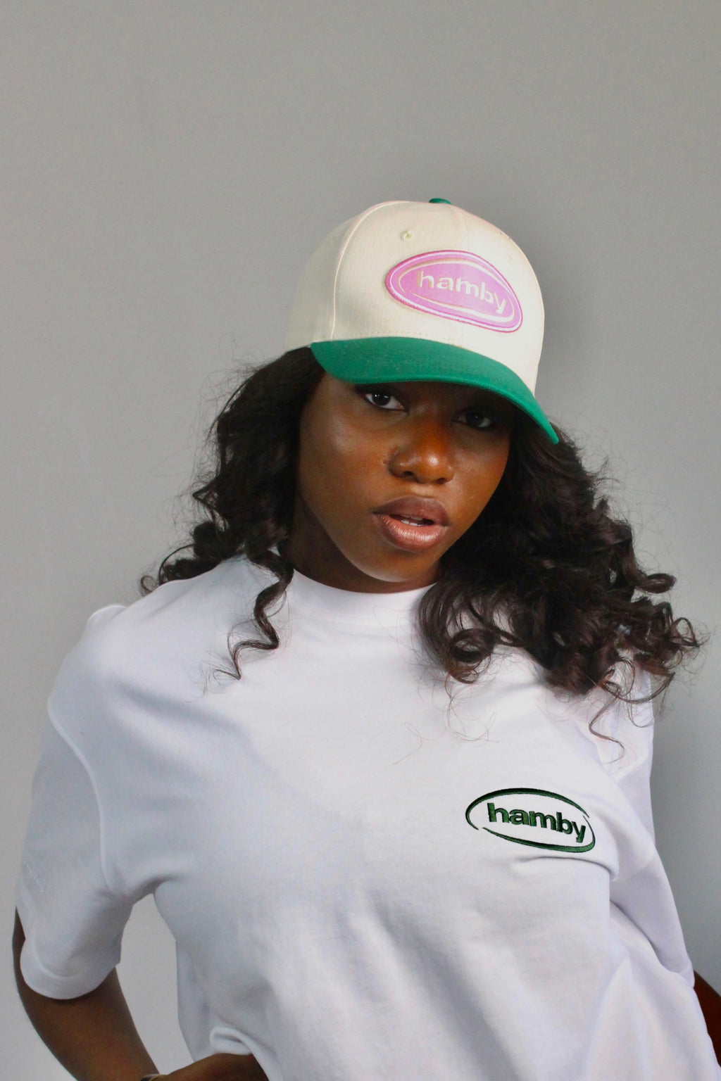 Model wearing a hamby SnapBack baseball cap. Cream cap with pink logo patch and green visor. ‘Create your own luck’ embroidered onto the left panel. 