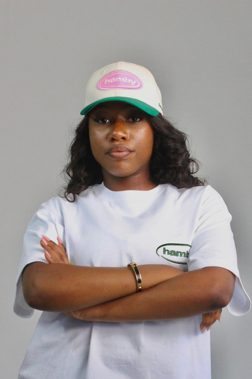 Model wearing a hamby SnapBack baseball cap. Cream cap with pink logo patch and green visor. ‘Create your own luck’ embroidered onto the left panel. 