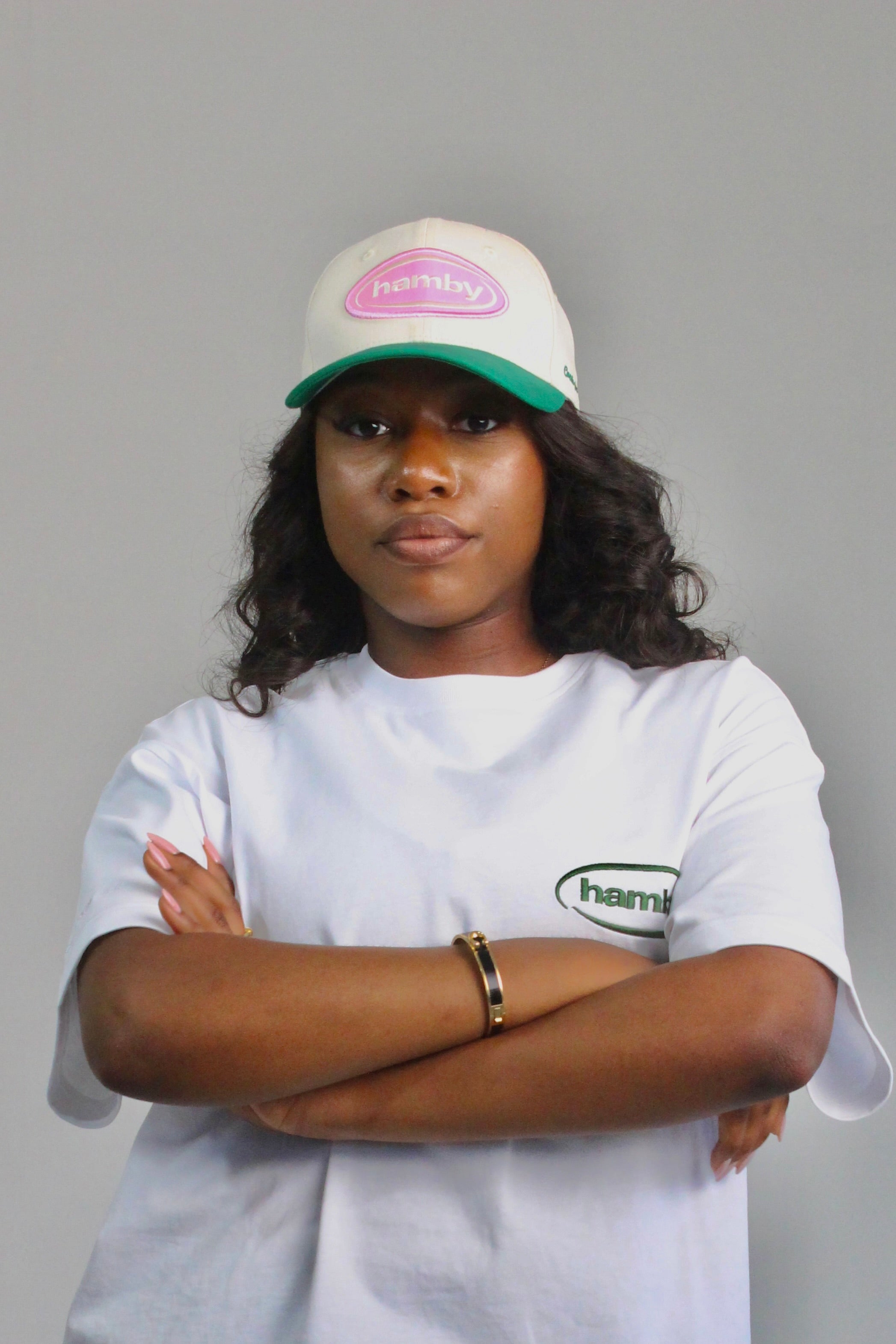 Model wearing a hamby SnapBack baseball cap. Cream cap with pink logo patch and green visor. ‘Create your own luck’ embroidered onto the left panel. 