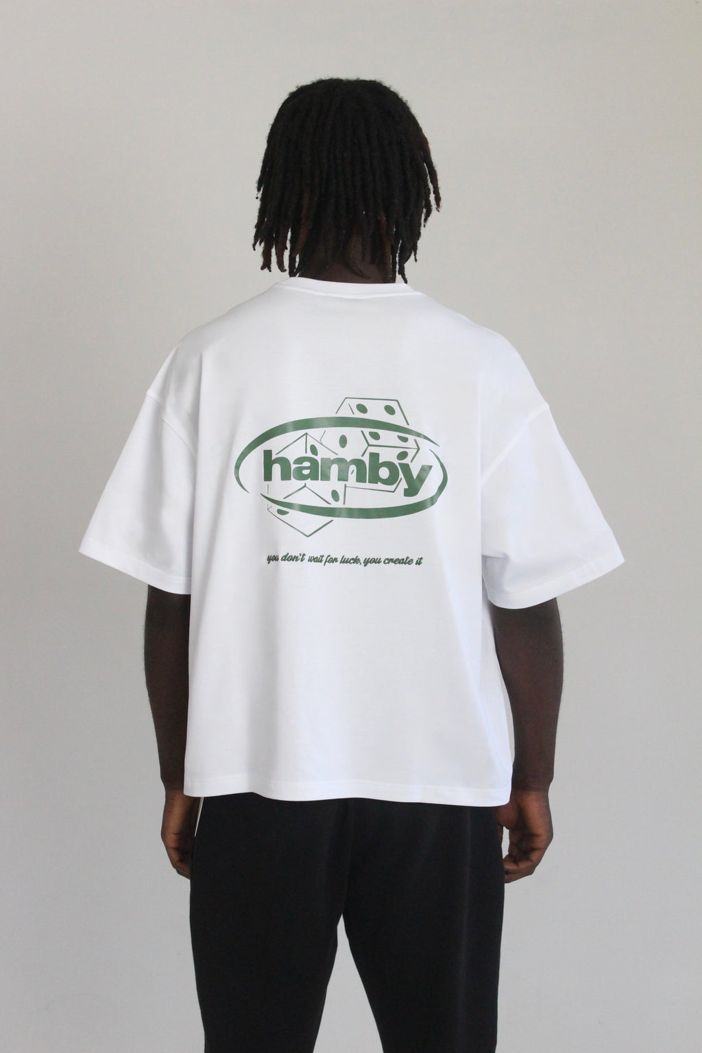 Model wearing white t-shirt with hamby logo and dice screen printed onto back of the tee. Embroidered quote underneath the print. Quote says ‘you don’t wait for luck, you create it’