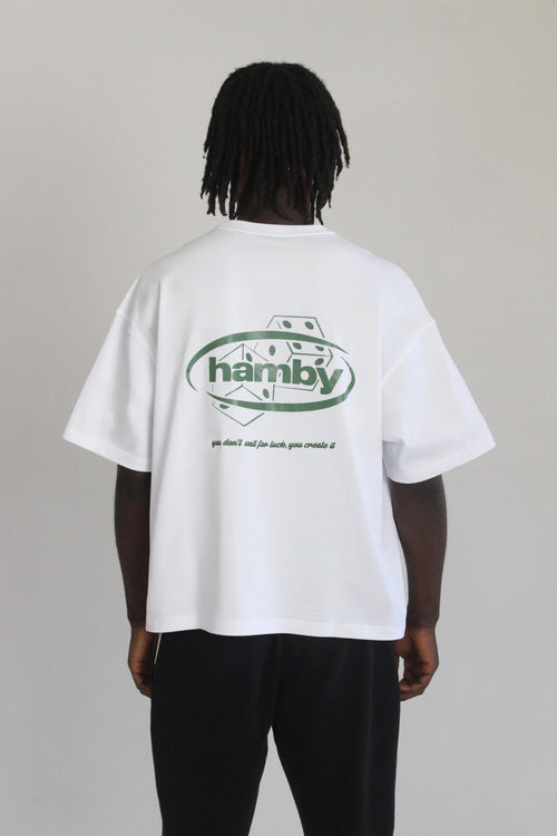 Model wearing white t-shirt with hamby logo and dice screen printed onto back of the tee. Embroidered quote underneath the print. Quote says ‘you don’t wait for luck, you create it’