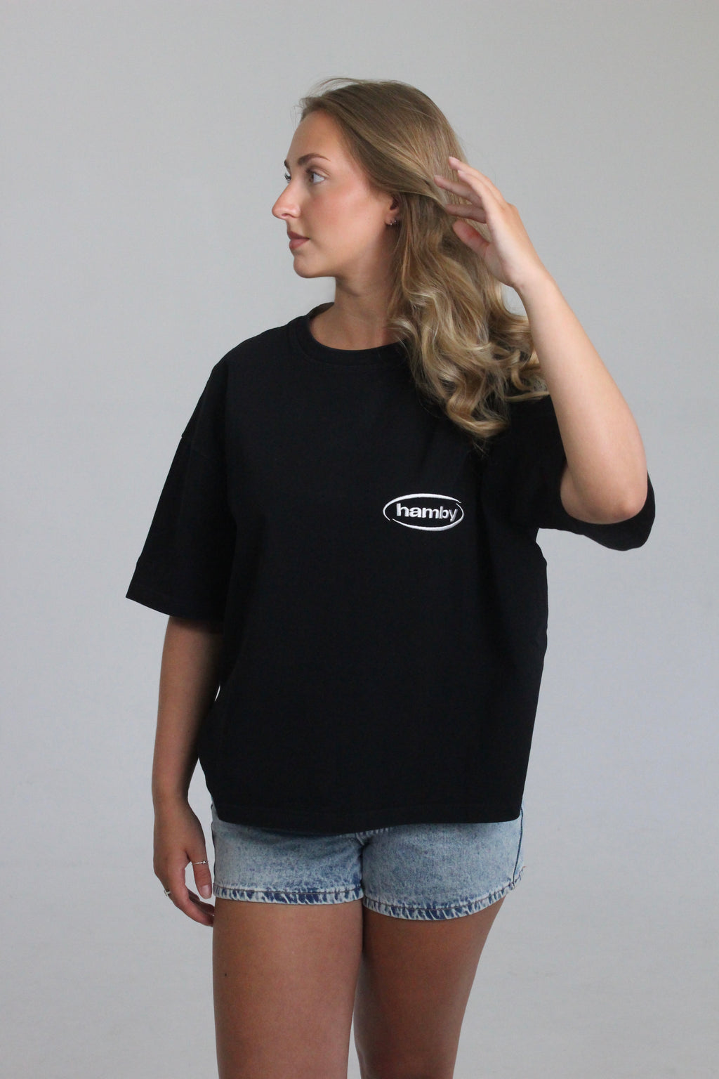 Model wearing boxy oversize hamby black t-shirt with hamby logo embroidered on the front left chest in white. 
